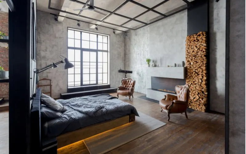 Industrial style interior design in a loft-style home with natural wood floors, concrete walls, and metal accents with a wood burning stove across from the bed