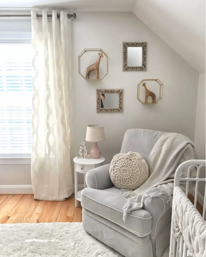 Warm decor in a transitional style home's baby nursery featuring very light green walls, white sheer curtains, and white trim with light brown or tan hardwood floors