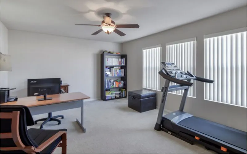 Home workout room with a treadmill sitting next to a desk and bookshelf