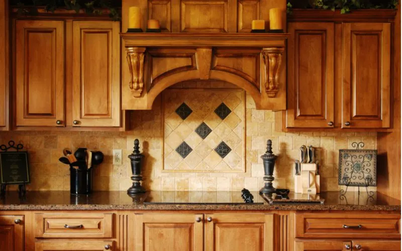 Honey maple kitchen cabinets with tan travertine backsplash designed in an ornate way