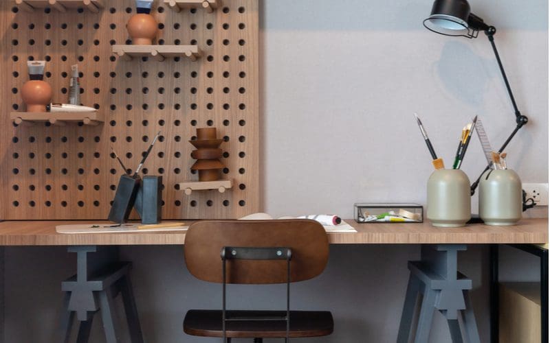 Teen boys room decorating idea using a pegboard wall above a simple wooden desk made of wood horses on which sits a black lamp