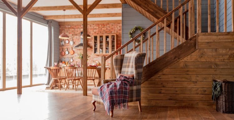 Cabin interior with wood-paneled walls and natural exposed wood beams and an open floorplan that opens to the kitchen