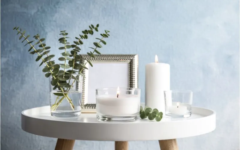 White candles sit on a modern white end table in the transitional home style with wooden legs in a teal textured room