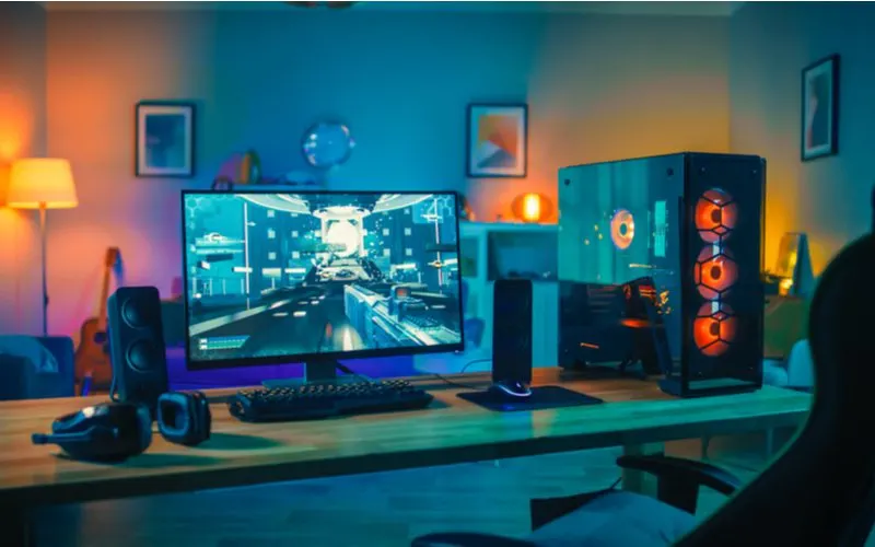 Gaming setup idea featuring a desk in the middle of a living room with yellow accent lamps and speakers next to the computer module and mouse