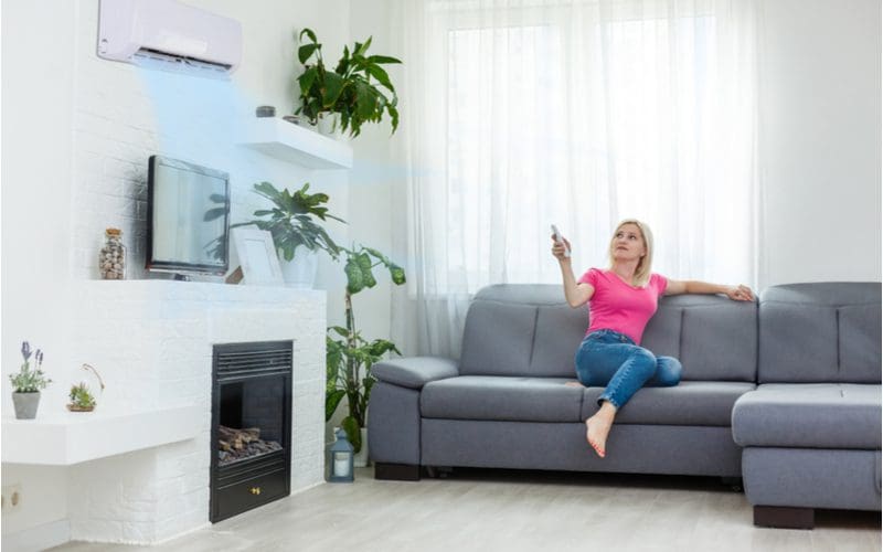 Woman using a wall-mounted ac unit by clicking a remote