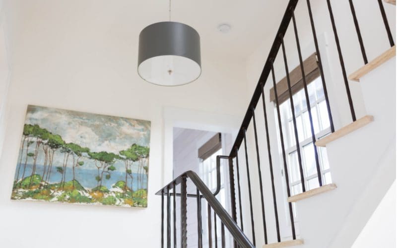 Stair decorating idea featuring a hand-painted canvas of an ocean landscape hung on a white wall with a black railing with natural light wood stairs
