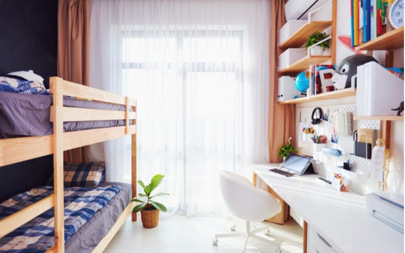 Teen boys bedroom decorating idea using natural wood floating shelves and bunk beds next to a window with sheer curtains