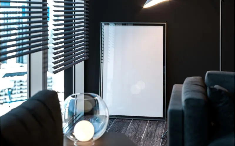 For a piece on hanging heavy pictures without nails, a big frame with only a white piece of paper on the inside sits resting against a black wall