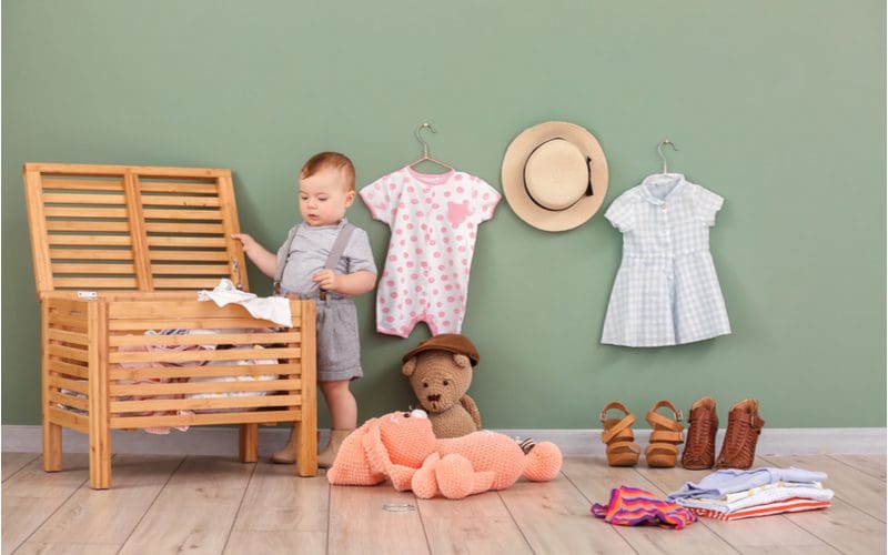 As a living room toy storage idea, a natural wood slatted toy chest holds various clothes and toys being pulled out by a little boy