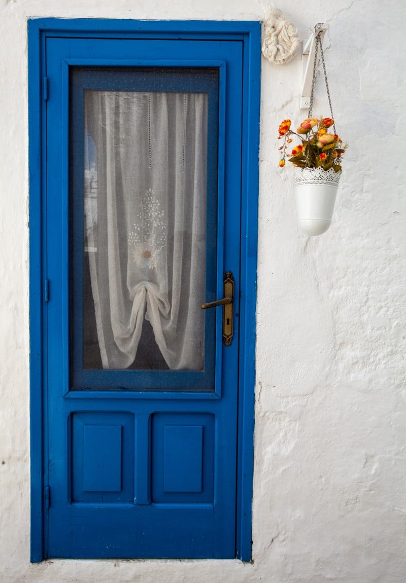 Old-fashioned, Lacy, Hanging Entryway Planter Idea outside a stucco home with a blue door