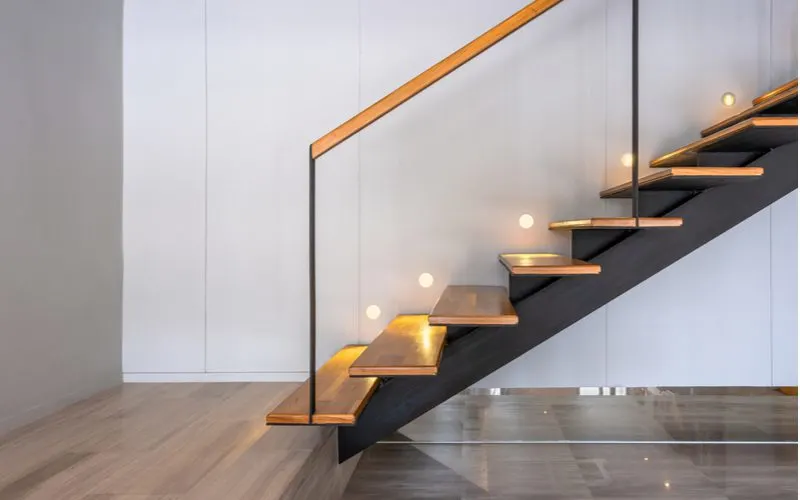 Decorating idea for stairs to incorporate lighting into the wall to illuminate each stair as shown in a floating wooden staircase with white walls