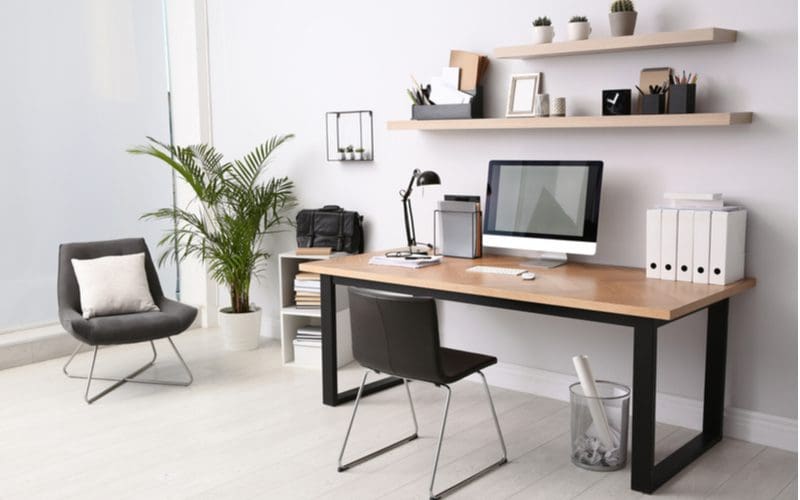 Bachelor pad home office idea with floating wooden shelves, a wooden desk with square metal legs, and plush chairs with a light grey floor