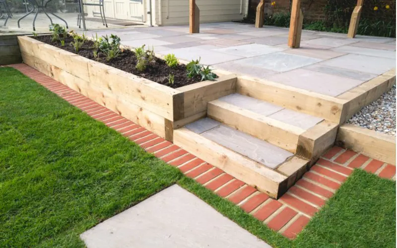 Brick Mowing Strip around a cedar plank-lined concrete patio with built in flower beds for a piece on lawn edging ideas