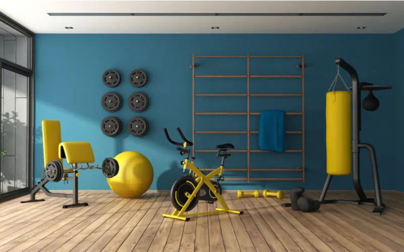 Bachelor pad idea with a yellow workout bike, a yellow punching bag, and a yellow weight bench in a painted teal room