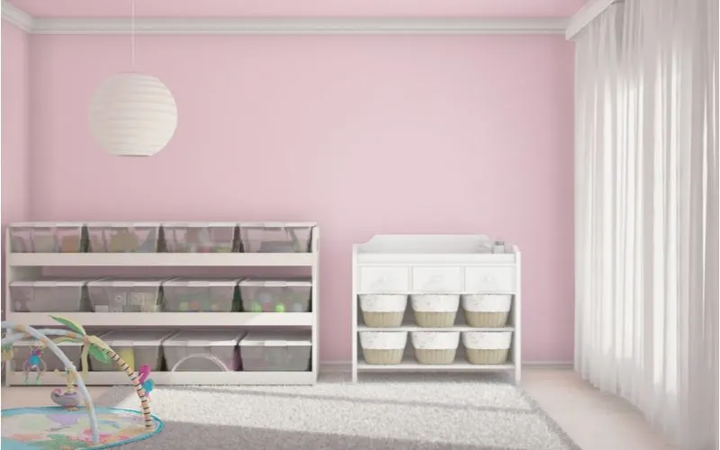 Monochromatic living room toy storage idea featuring rows of shelves with plastic bins and wicker baskets below in a soft pink room