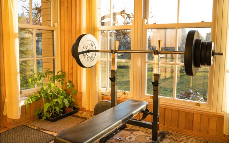 Breakfast nook with a weight bench in it with lots of heavy weights on the barbell overlooking the yard