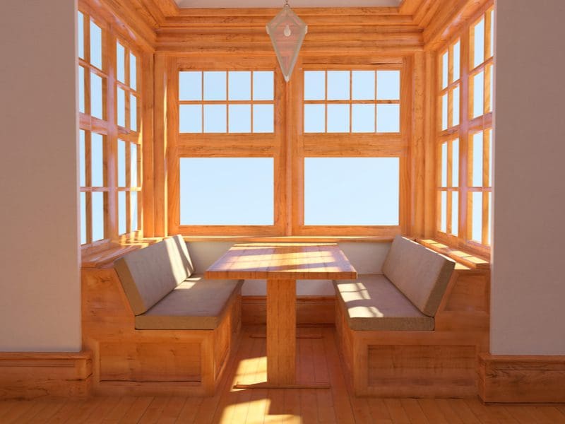 Sunroom Add-On Breakfast Nook made of natural wood benches and a t-style table and surrounded by windows
