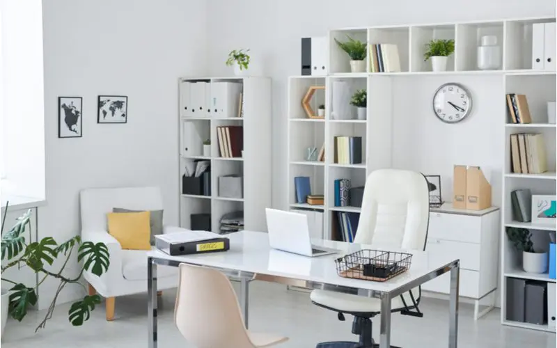 White and bright home office design idea with lots of modular shelves on the back wall behind the desk and chair