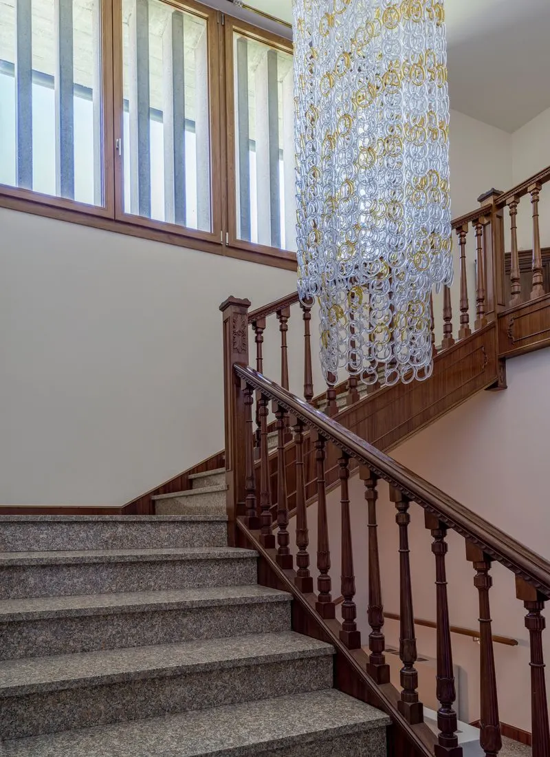 Decorating idea for stairs featuring a dark stained wood railing with carpeted stairs and a glass and metal chandelier as the decoration to bring life into the room