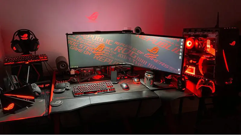 Gaming setup idea featuring a headphone stand on a desk that's black with all red accent lighting on the PCU, the controller, the headphones, keyboard, and ambient lighting on the wall