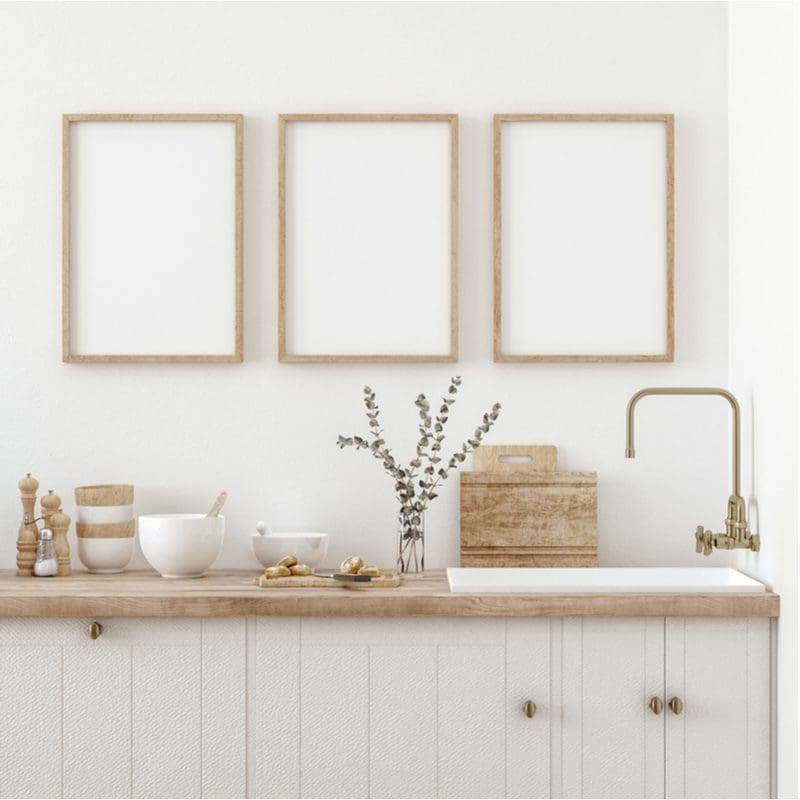 As an image for a piece on kitchen wall decor, a number of frames in natural wood sit above a butcher block countertop