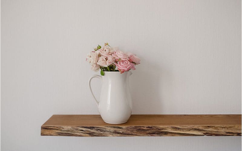 Floating modern rustic bathroom shelf holding a flower pot on it and attached to a white wall