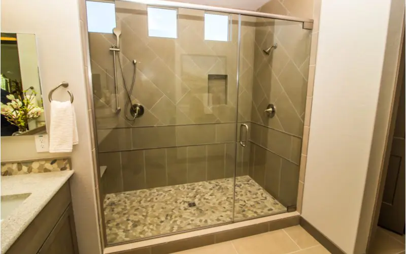 Large glass doored shower with a floating shower bench and two separate heads on either side