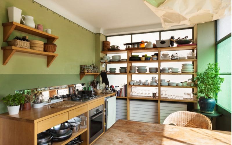 Loft style rustic kitchen cabinets with green walls next to a large exposed shelving unit on which several pieces of pottery and plateware sit