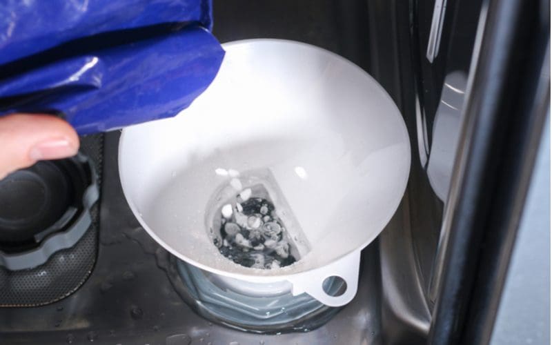 Guy putting drano in a dishwasher's drain using gloves and a funnel, which you should NEVER do