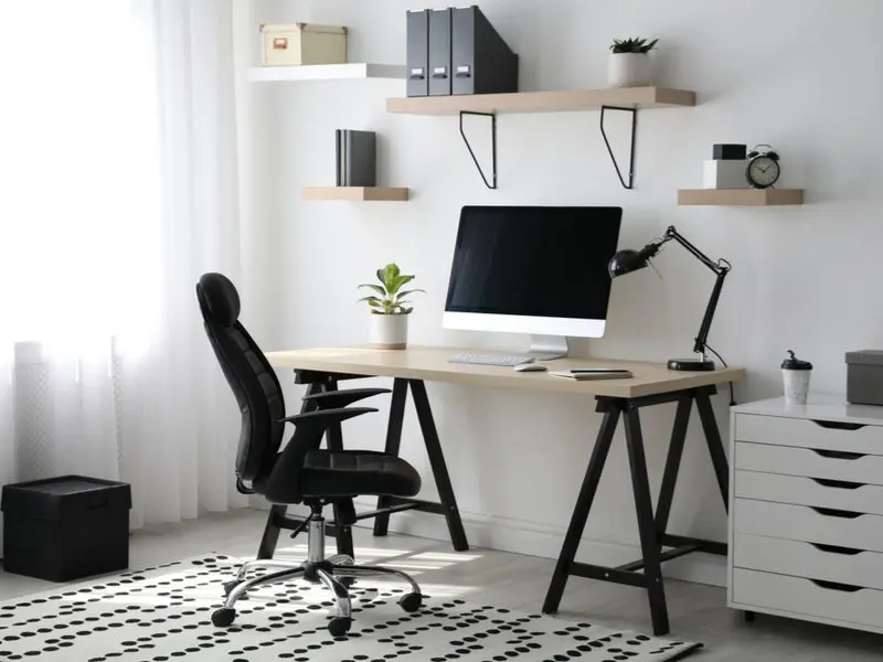 Home office design idea featuring an ergonomic chair in front of a easel-style desk with black legs and a natural wooden top below floating shelves of various colors and lengths
