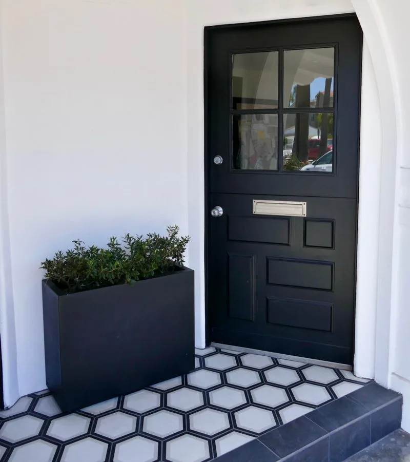 Front door entryway featuring a tiled floor made of gray hex tile with gunmetal tile accents next to an entryway planter idea made of black wood