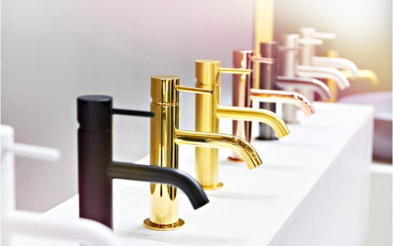 A number of single-handle bathroom faucets in various colors and finishes sit in a row on a display for a piece on faucet brands