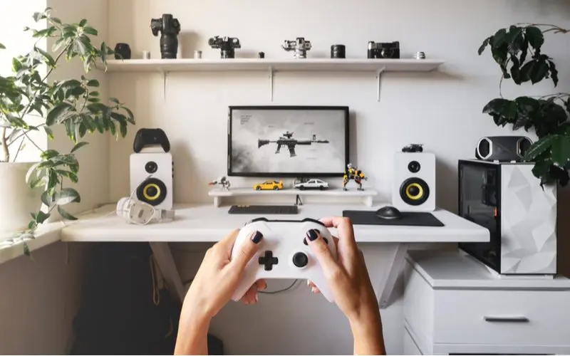 Gaming setup idea as depicted from a player's POV with a floating white shelf desk and speakers and a white PCU below cameras that sit on a floating shelf above the single monitor