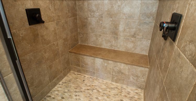 Featured image for a piece on shower bench size with a bench on one wall of a travertine tile shower