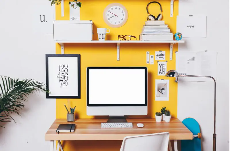 Home office design idea with white metal and wooden shelves attached to a yellow wall above a wooden and white desk
