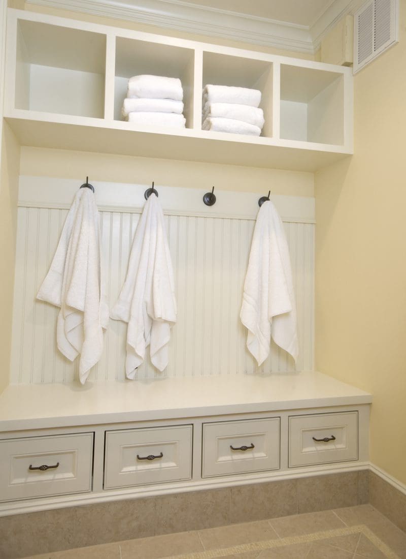 Mudroom style locker room with a bunch of white towels hanging from black towel hooks for a piece on small home gyms