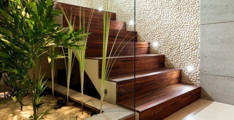 Stair decorating idea featuring natural wood stairs next to black rock wall texture and a glass half-wall