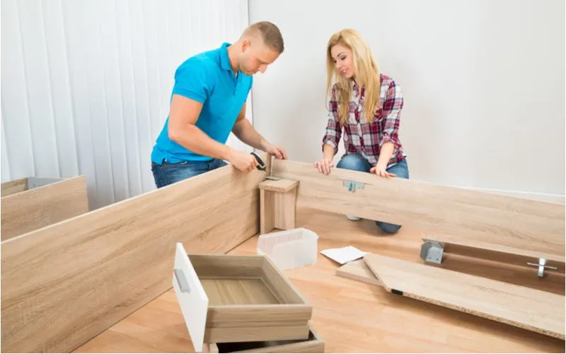 Couple putting together the various parts of a bed staring with the frame and including the drawers, the headboard, and more