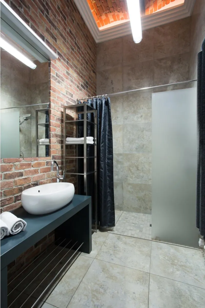 Industrial styling featured in a washroom or bathroom with natural brick ceilings, metal shelves, and dark blue vanities and shower curtains
