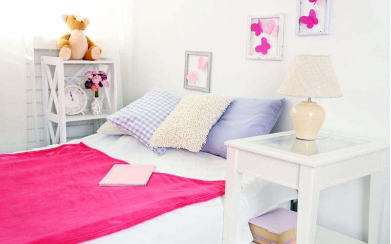 Cute room for girls with a pink bedspread, teddy bear, and purple butterflies made from paper in rustic grey wooden picture frames