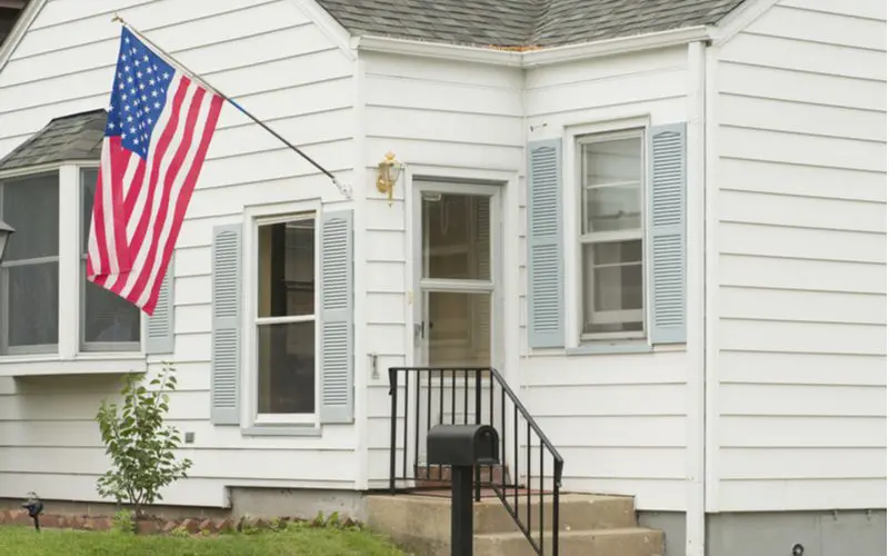 Image of a front porch from which hangs an American Flag at full staff