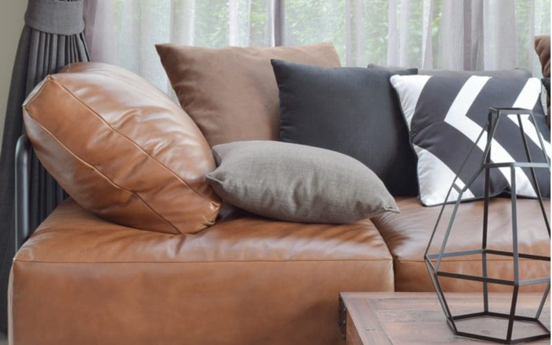 Light brown leather sofa with black, brown, and grey/white throw pillows sitting on the top