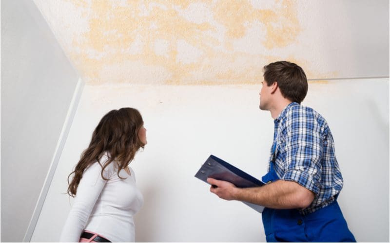 Worker with a soccer mom in a white shirt and pink pants looking up at the ceiling at the water stain on the ceiling
