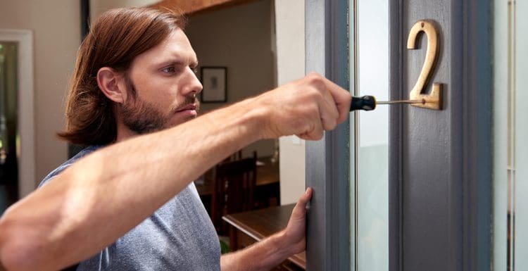 Guy with long hair using a screwdriver to install a house number after reading our guide to house number ideas