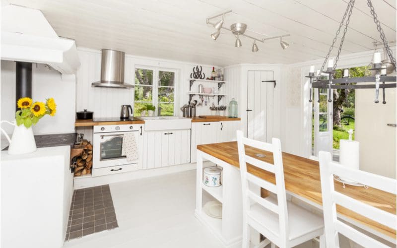 Clean white cottage interior with white cabinets, white paneled walls and ceilings, and white tile floor with the only accents being natural stained wooden butcher block counters and tabletops