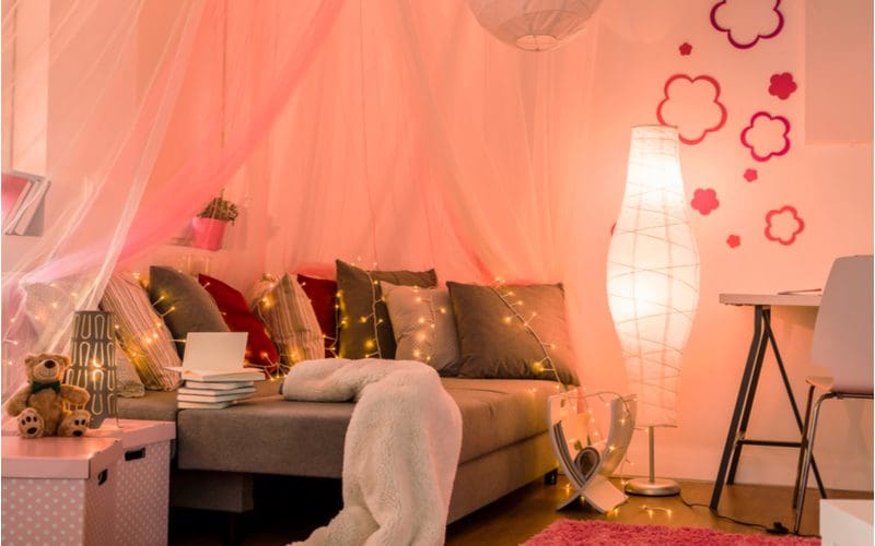 Cute room for girls with ambient lighting, flower wall decals, a hanging paper light fixture, and fairy lighting draped over the couch