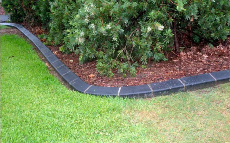 Curved Black Bricks laid end to end separating the dark brown mulch from the lush green yard for a roundup of lawn edging ideas