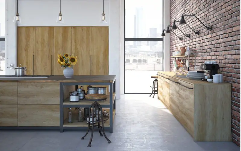 Rustic cabinets with metal shelves built in using the industrial style design aesthetic next to a brick wall with a big floor to ceiling window nearby
