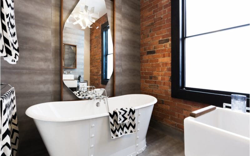 Brick accent walls next to a grey industrial-style bathroom wall with black trim and an above-ground tub