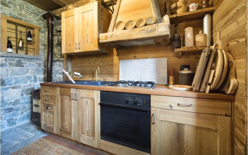 Wood burning stove heats a kitchen that has rustic cabinets made of unstained wood with wooden butcher block counters and a wood stove vent for a wood-on-wood look
